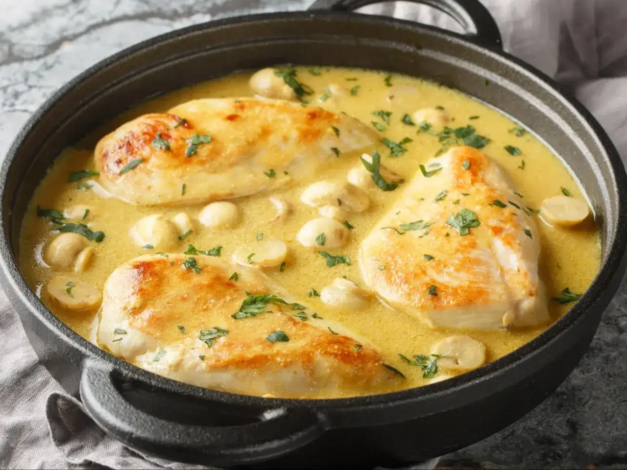 Soczysty filet drobiowy w kremowym sosie z pieczarkami, posypany natką pietruszki, podany w czarnym naczyniu.