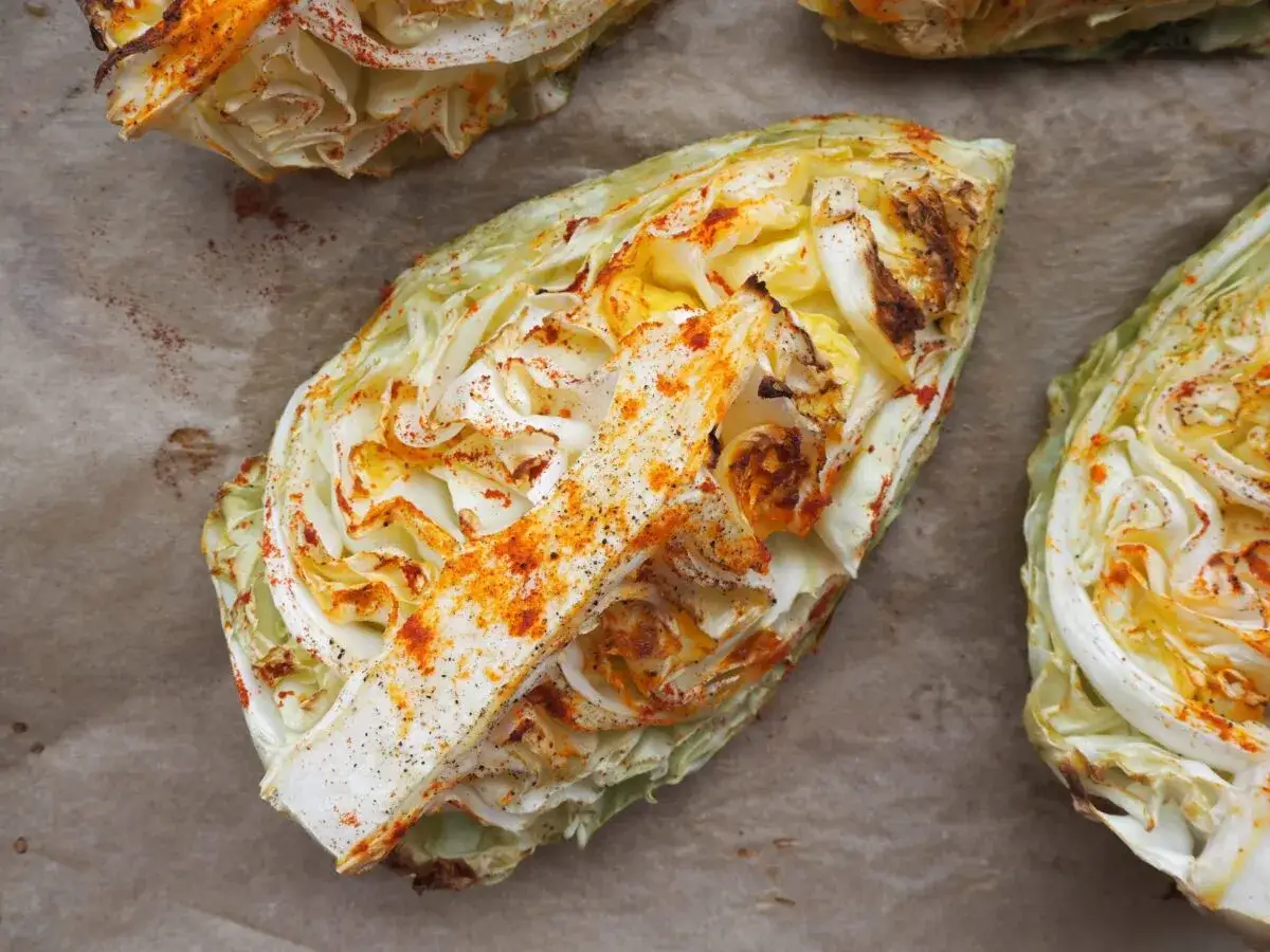 Pieczona kapusta, pokrojona w ćwiartki i posypana papryką, wygląda apetycznie na papierze do pieczenia.